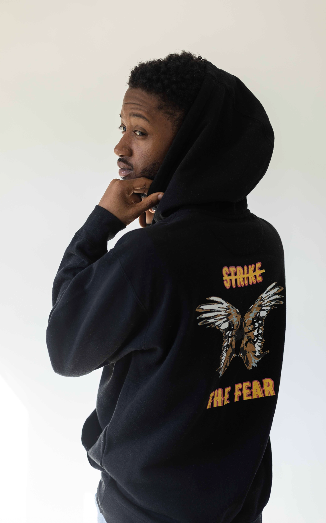 Person wearing a black hoodie with a design and text on the back against a white background